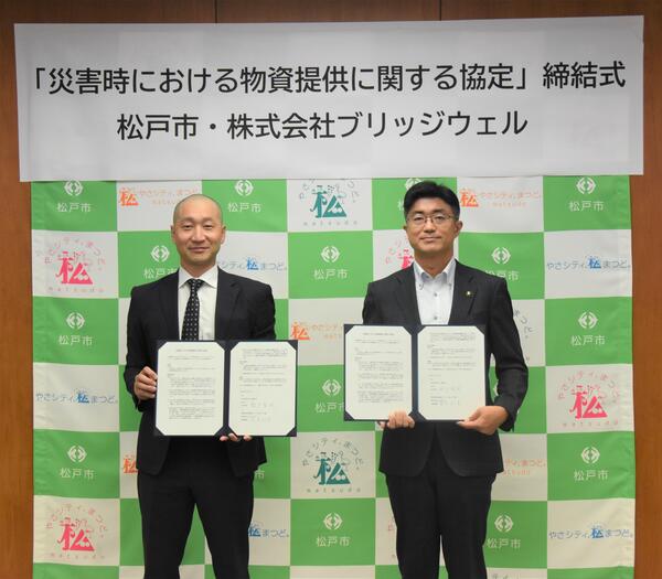 協定書を手に持って並ぶ松戸市長と筒井代表取締役