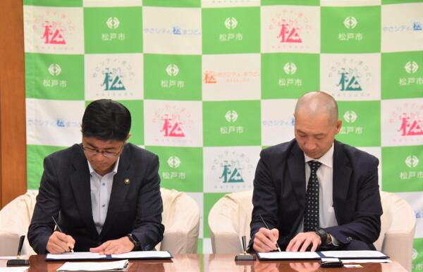 締結書にサインする松戸市長と筒井代表取締役