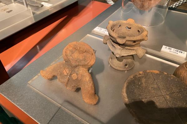 常設展示室で展示中の異形台付土器と土偶（いずれも貝の花遺跡出土）の画像