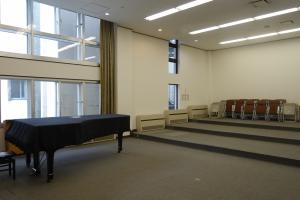 303音楽室ピアノ付近の写真です。手前にピアノがあり、奥にパイプいすが立てかけてあります。